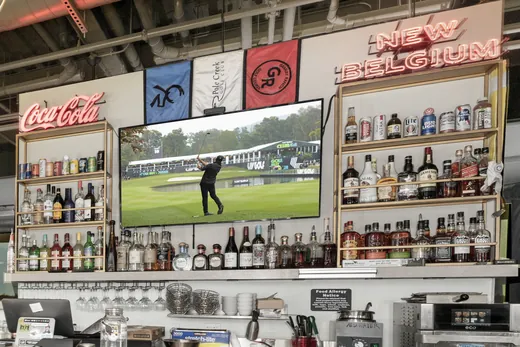 The back bar: bottles on open shelves, a New Belgium neon and golf on the TV.