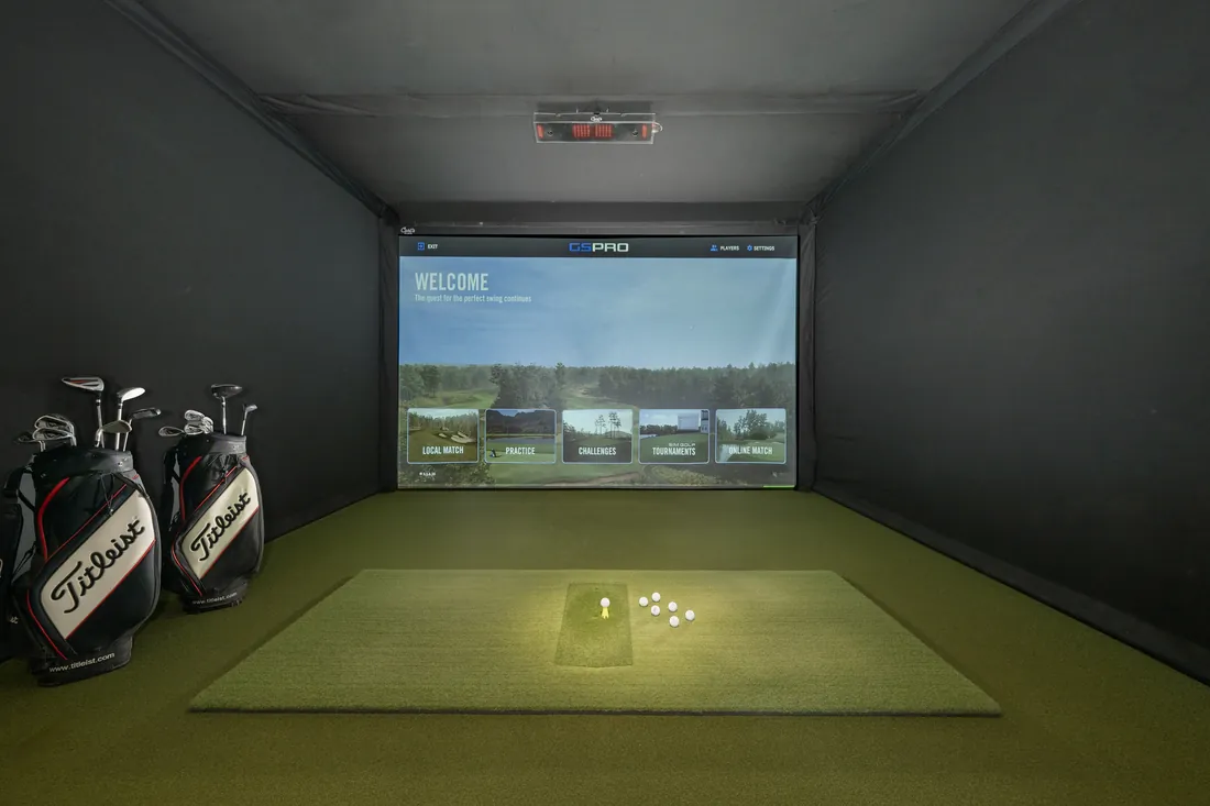 A bay at the Birdie Lounge, balls teed up on the mat and the course on the big screen.