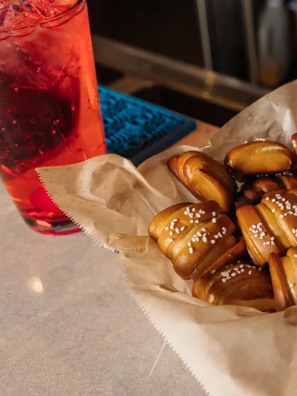A red cocktail next to a basket of pretzel bites on the bar.