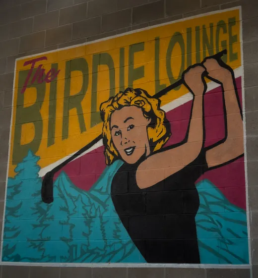 The Birdie Lounge mural: a retro golfer mid-swing in front of mountains and pines, the name painted in big letters above her.