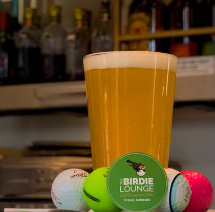 A cold pint on the bar with golf balls and a Birdie Lounge sticker.